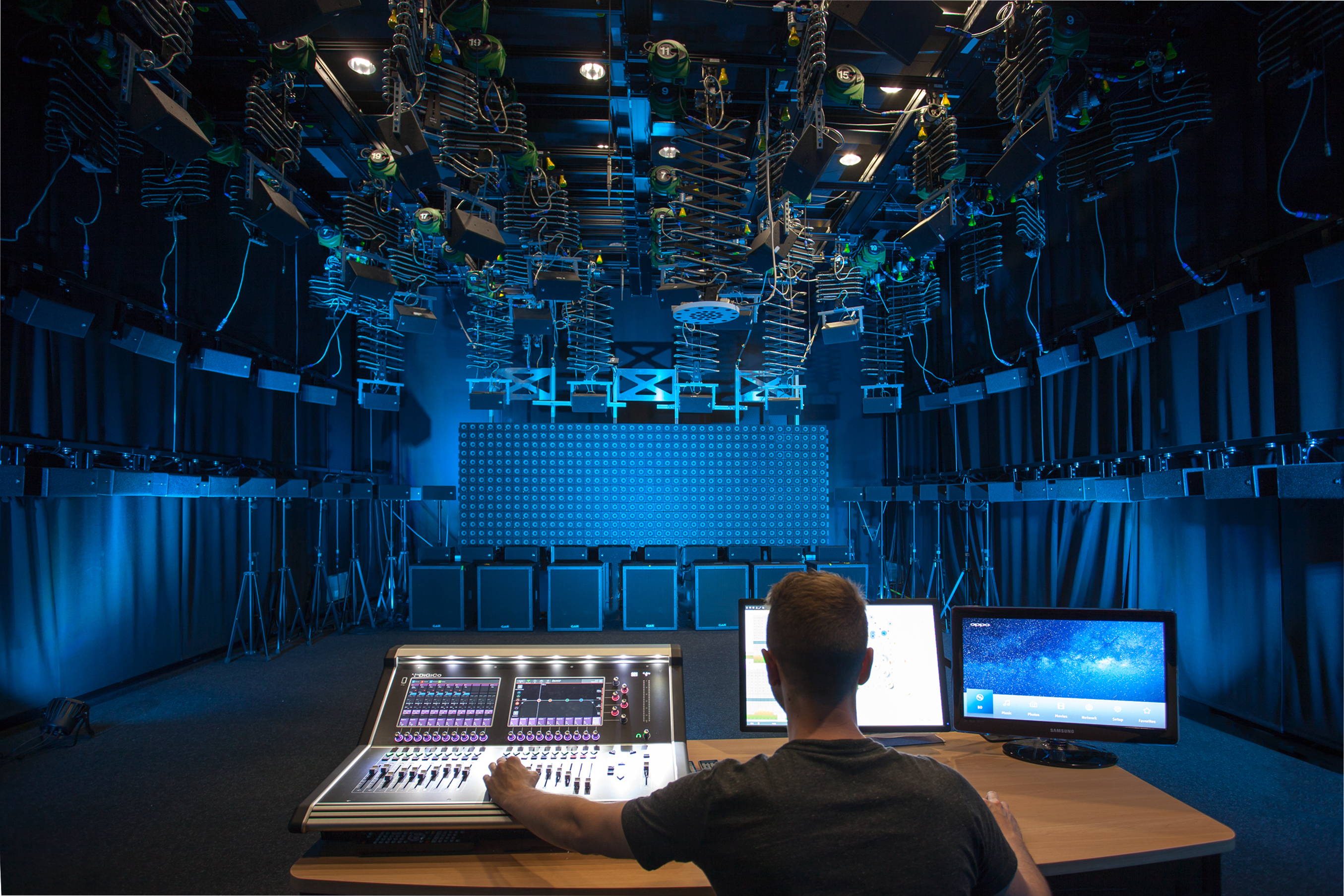Man at the mixing desk in a room full of speakers.